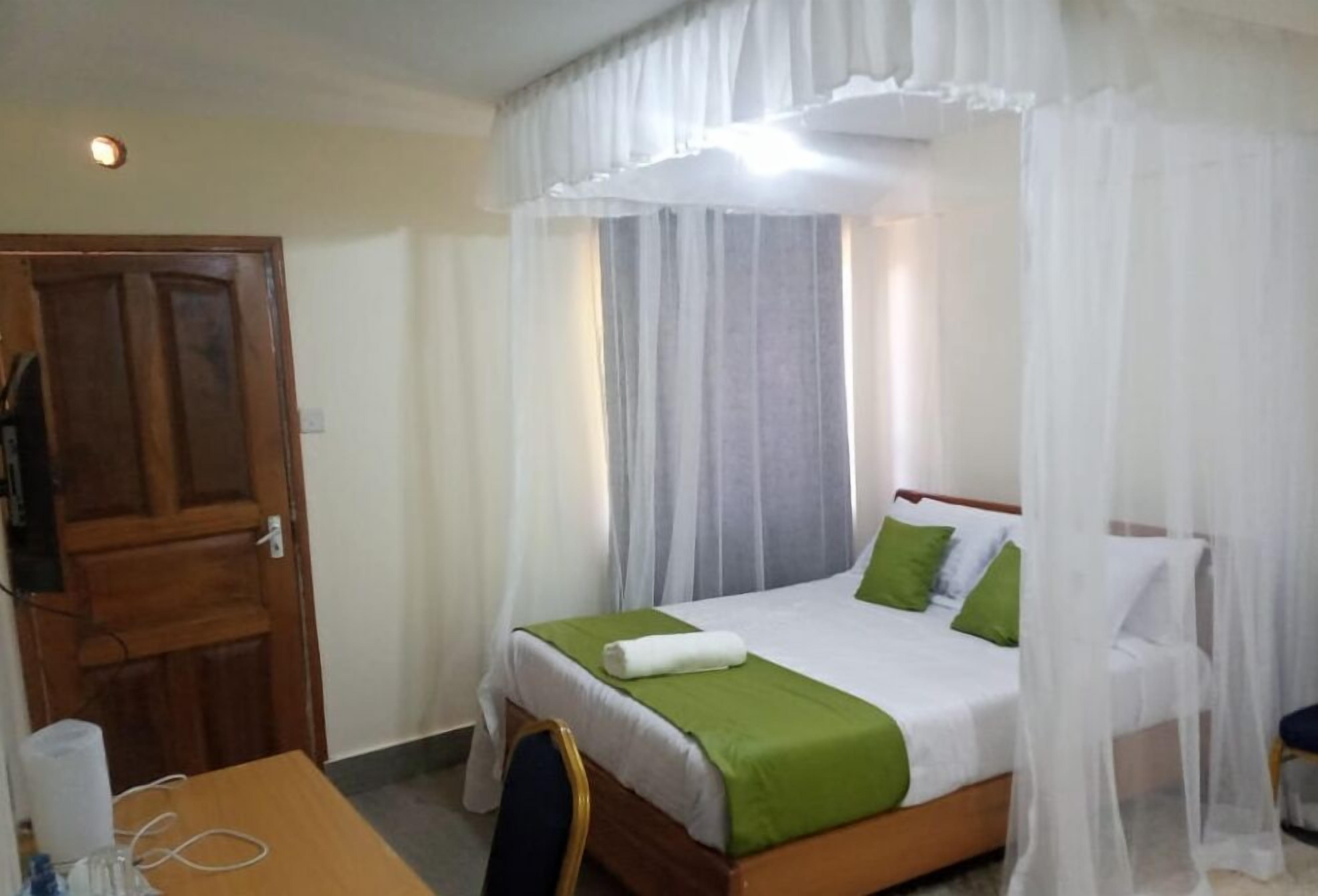 A neatly made bed with green pillows, a white canopy, and a wooden headboard.