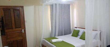 A neatly made bed with green pillows, a white canopy, and a wooden headboard.