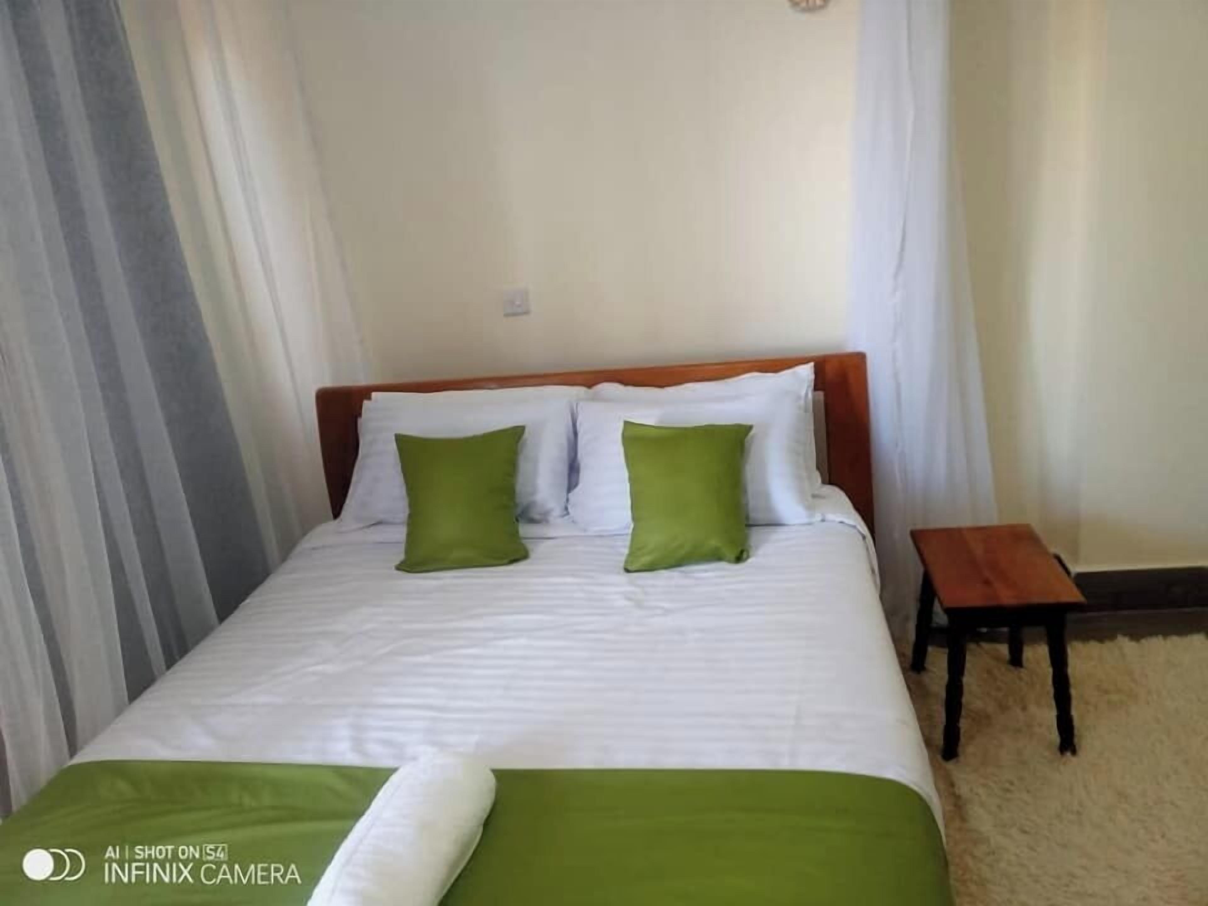 A neatly made bed with white linens and two green pillows, a wooden headboard, and a small wooden nightstand beside it.