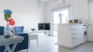 Un salon moderne avec un canapé bleu, une table basse blanche et un téléviseur. Il y a également un coin cuisine avec un lave-linge et une table à manger avec des chaises.