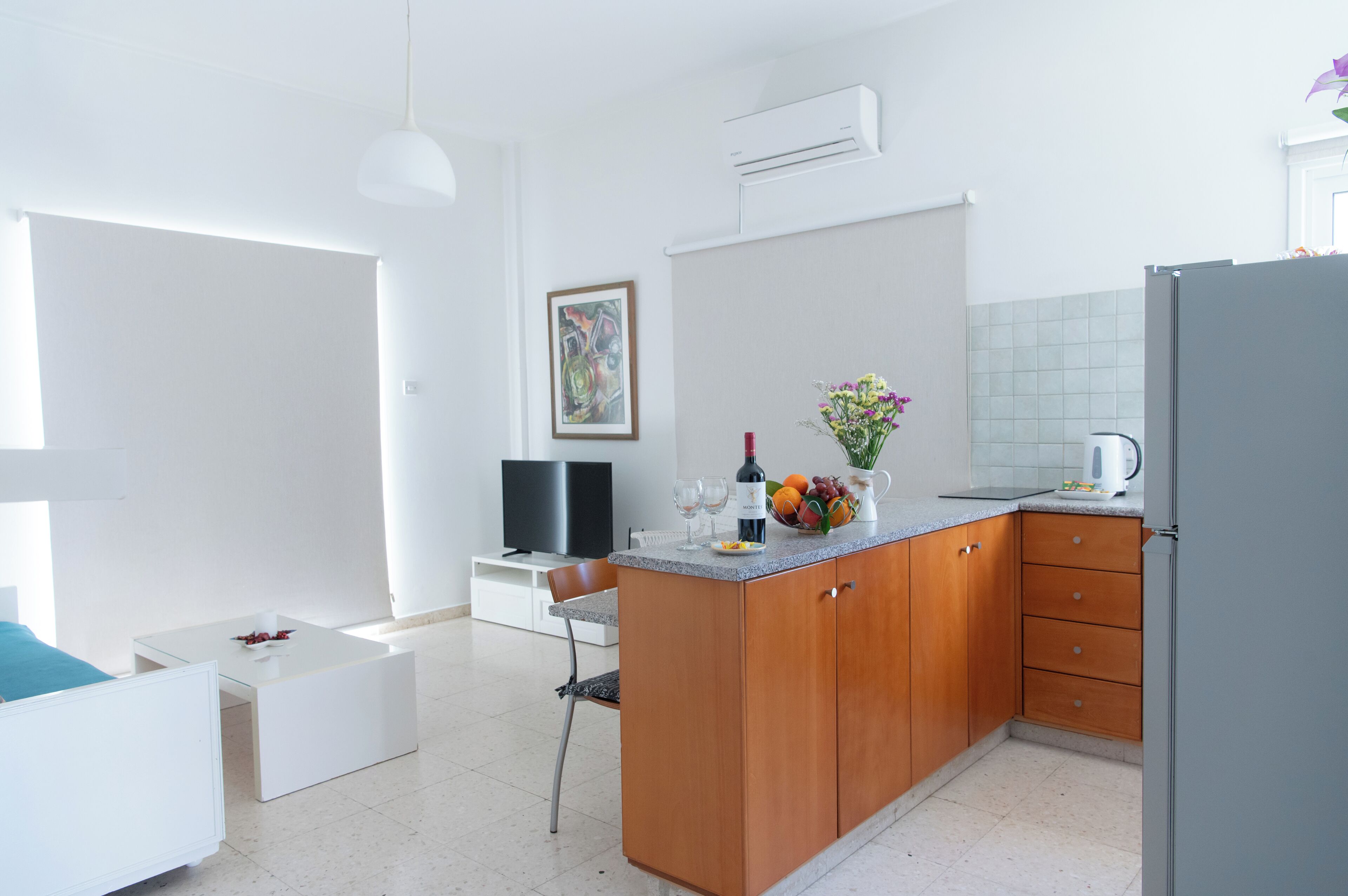 A modern kitchen with wooden cabinets, a countertop with a vase of flowers, and a television in the background.
