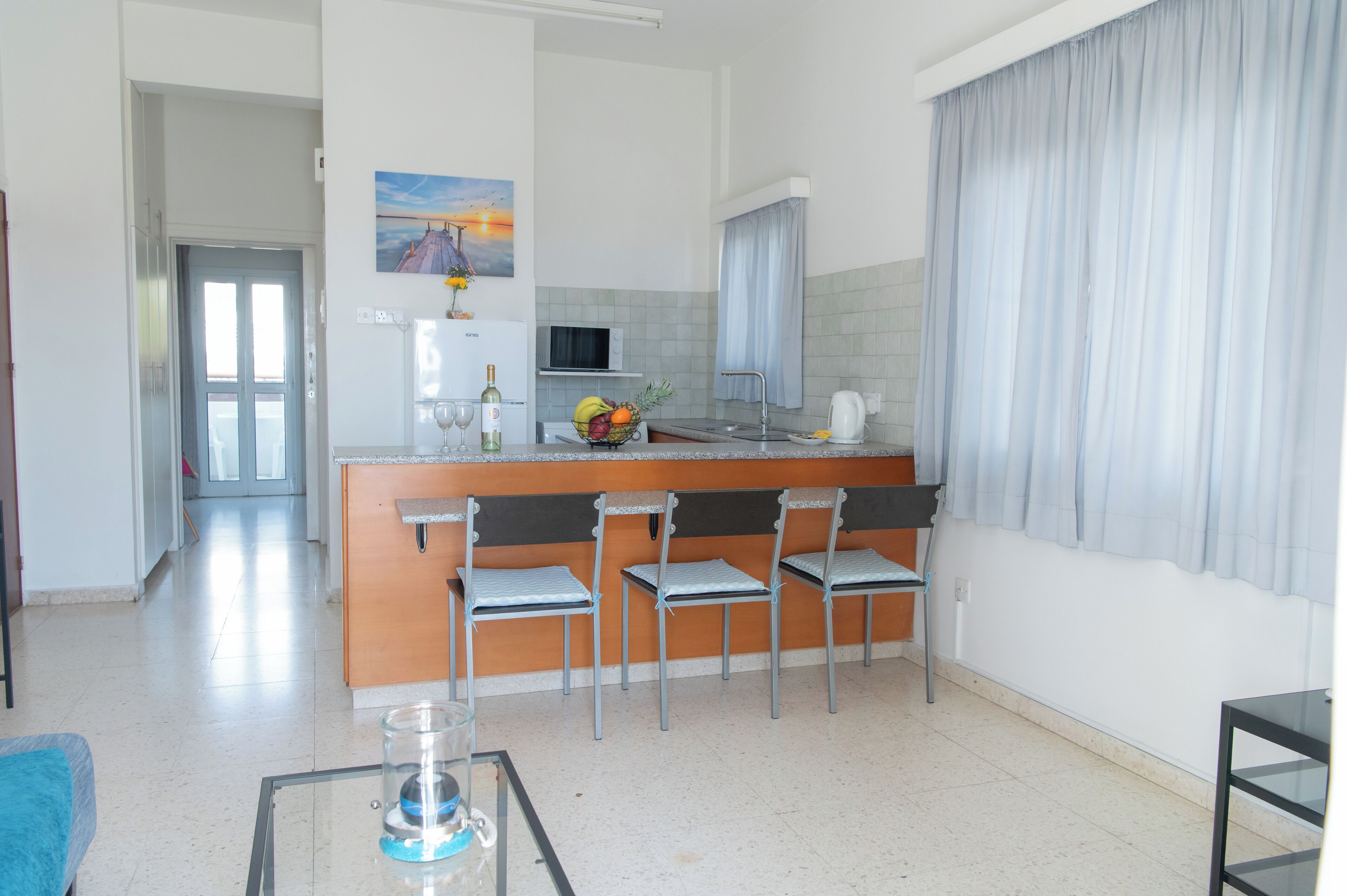 A modern kitchen with a central island, bar stools, a microwave, and a fruit bowl.