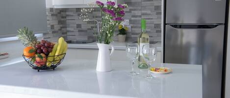A kitchen counter with a fruit basket, a vase with flowers, wine glasses, and a bottle.