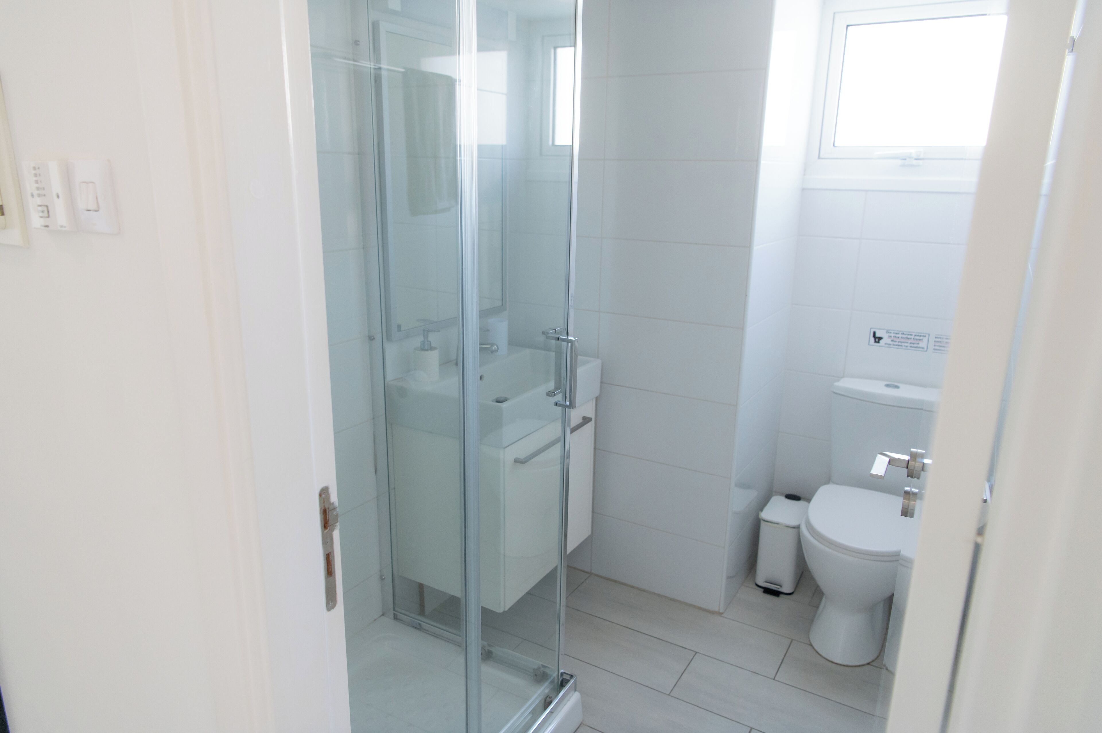 Un baño moderno con cabina de ducha de vidrio, un inodoro y un pequeño cubo de basura.