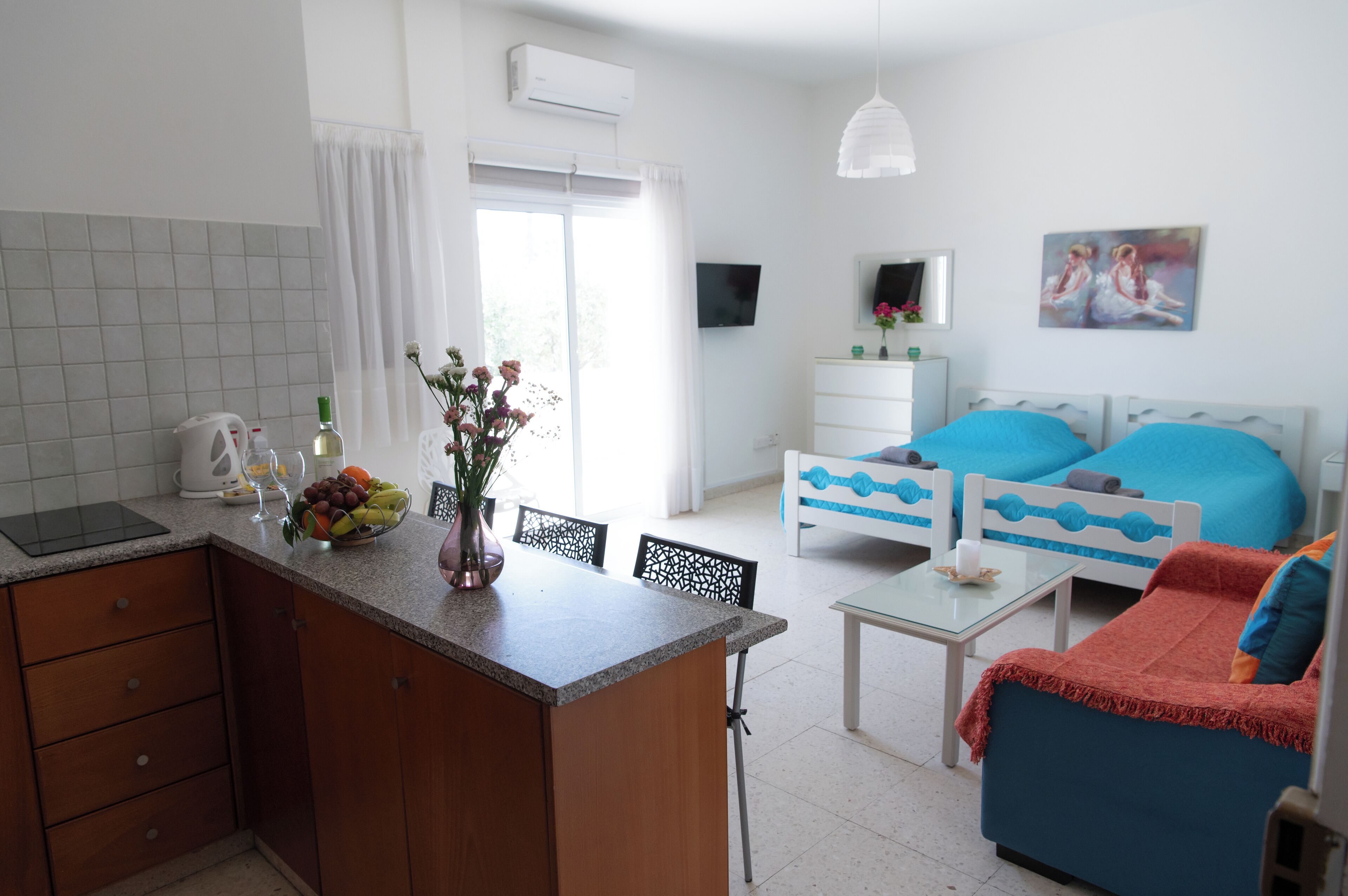 Una cocina moderna con comedor, una mesita pequeña y un sofá. Se aprecia una ventana con cortinas, un televisor de pantalla plana y un cuadro en la pared.