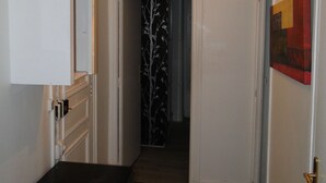 Un couloir avec un plancher en bois, une porte blanche sur la droite et une porte à motifs noir et blanc sur la gauche.