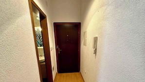 A narrow hallway with wooden flooring and white textured walls. A dark wooden door is at the end of the hallway. - App Vida (Crikvenica)