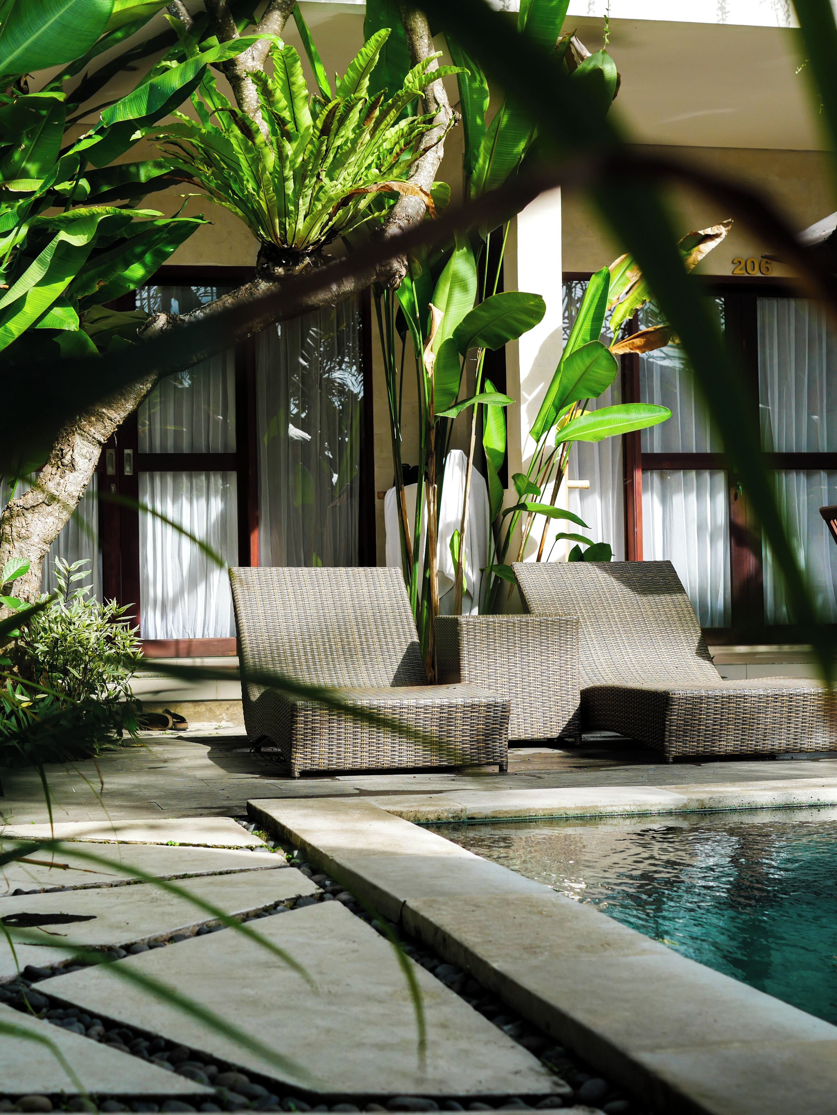 Zona junto a la piscina con sillones de mimbre y un camino de hormigón que conduce al agua.