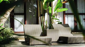 Zona junto a la piscina con sillones de mimbre y un camino de hormigón que conduce al agua.