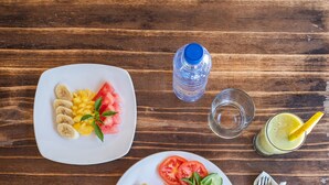 Zwei Teller mit Essen, eine Wasserflasche, ein Glas und ein Servietttuch auf einem Holztisch.