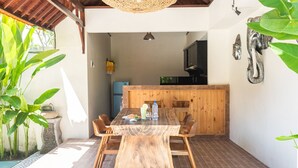 Ein Essbereich mit Holztisch und Stühlen, im Hintergrund eine Küche und tropische Pflanzen.