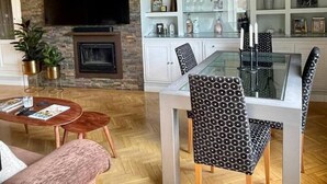 Ein modernes Wohnzimmer mit Kamin, einer Essecke mit Glastisch und einem an der Wand befestigten Fernseher.