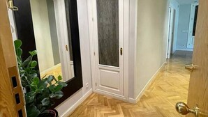 Ein Flur mit einem Fischgrätparkett aus Holz, einem großen Spiegel und einer Tür mit satiniertem Glas.