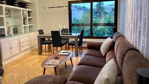 Ein modernes Wohnzimmer mit großem Fenster, einer Couch, einem Esstisch mit Stühlen und Einbauschränken.