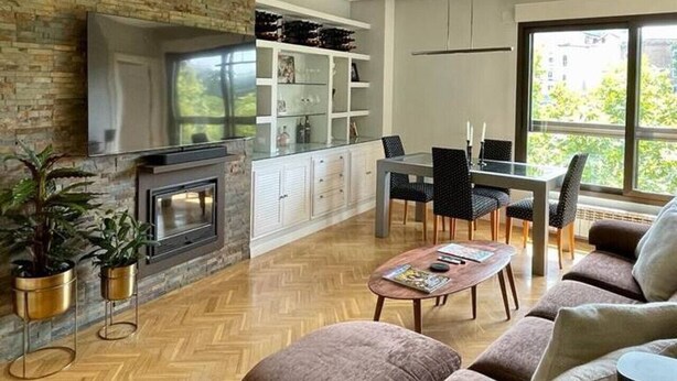 Ein modernes Wohnzimmer mit Kamin, Essbereich und großem Fenster mit Blick auf Grünflächen.