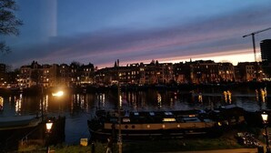 A waterfront cityscape at dusk with buildings reflecting on the water, a boat docked in the foreground, and a construction crane in the distance.