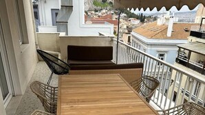 Et træbord med fire stole på en balkon med udsigt til bygninger.