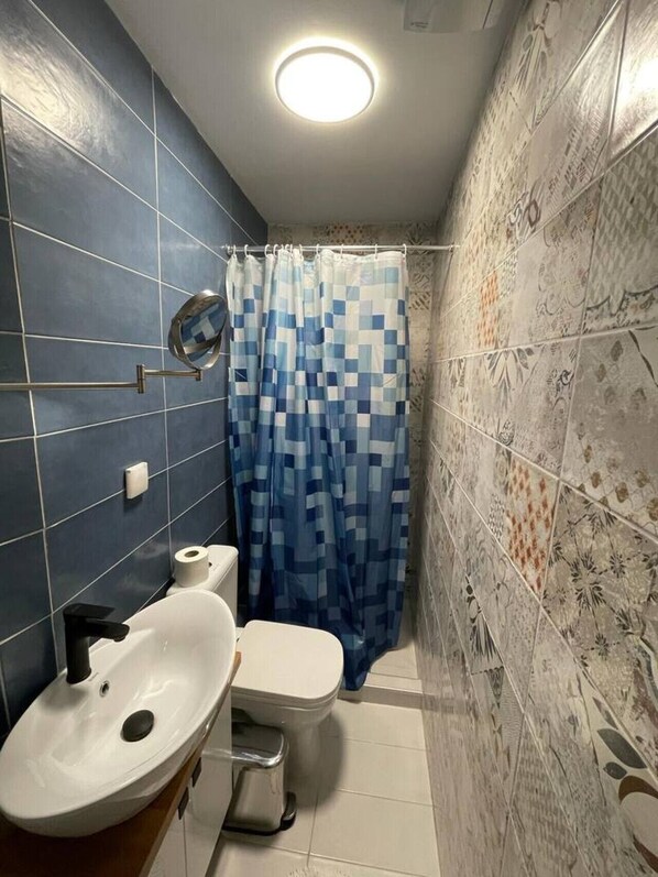 A bathroom with a white sink, a toilet, and a shower curtain with a blue pattern.