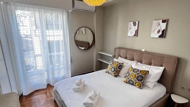 Un dormitorio ordenado con una cama grande, un espejo redondo y dos cuadros en la pared.