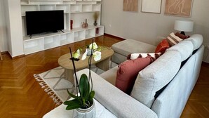 A modern living room with a large sofa, a coffee table, a TV, and a bookshelf. - Elegant Kolonaki Retreat | Sophisticated 2-Bedroom Apartment in Upscale Central Athens (Athina)