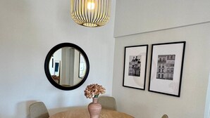 A dining area with a round wooden table, grey upholstered chairs, a woven rug, a hanging pendant light, a round mirror, and two framed pictures on the wall. - Sunset Sea View Pangrati Flat (Athina)