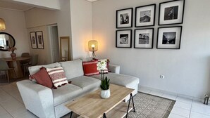 A modern living room with a grey sofa, a wooden coffee table, and a patterned rug. There are framed pictures on the wall and a lamp on the table. - Sunset Sea View Pangrati Flat (Athina)