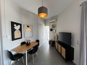 A modern dining area with a wooden table and black chairs, a black cabinet with a television, and artwork on the walls. - Rooftop Serenity in Pangrati | Jacuzzi, 2 Terraces & Acropolis Views in Central Athens (Athina)