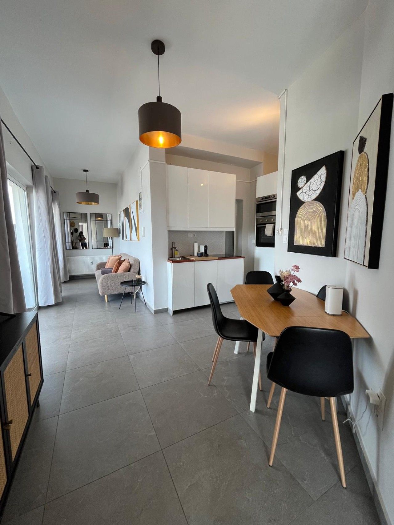 A modern kitchen with white cabinets, a dining area with a wooden table and black chairs, and artwork on the walls.