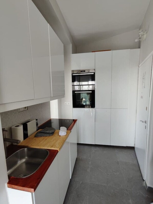 A compact kitchen with white cabinets, a stainless steel sink, and a wooden countertop. - Rooftop Serenity in Pangrati | Jacuzzi, 2 Terraces & Acropolis Views in Central Athens (Athina)