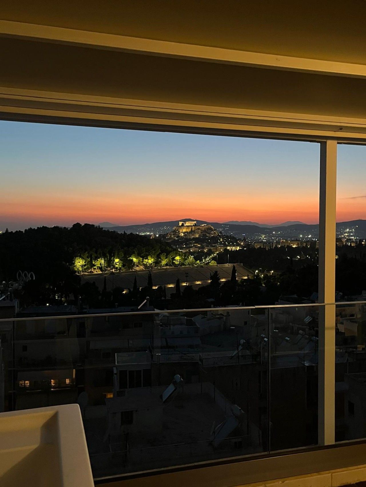 A view from a high-rise building at dusk, overlooking a cityscape with a prominent hill and distant mountains.