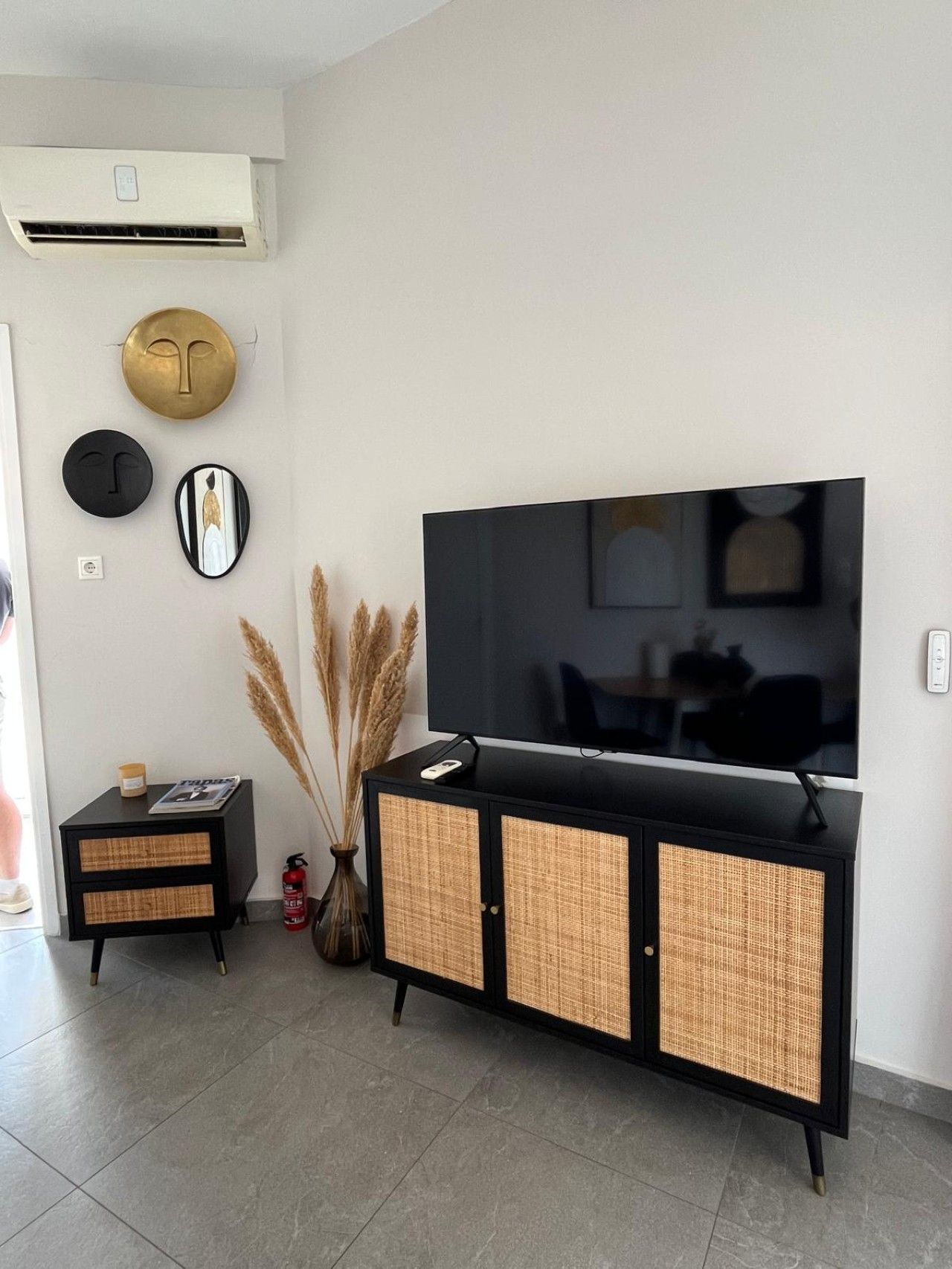 A living room with a flat-screen TV, a black cabinet with wicker doors, a small side table, and decorative wall art.