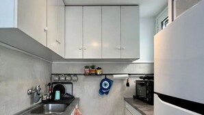 A compact kitchen with a sink, stove, and microwave. There are cabinets above the counter and a small shelf with potted plants. - Acropolis View Penthouse | Panoramic Terrace in the Heart of Athens (Athina)