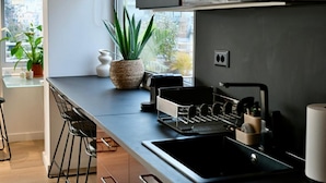 A modern kitchen with a built-in oven, a black countertop, bar stools, and a window with a view of buildings.