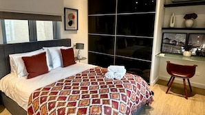 A modern bedroom with a large bed, a ceiling fan, a large window, and a desk area.