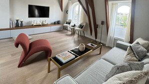 A spacious living room with a high ceiling, wooden beams, a large flat-screen TV, a sofa, a coffee table, and a unique red chair. - Grand Amstel Residence | Expansive Two-Story Riverfront Apartment in Central Amsterdam (Amsterdam)