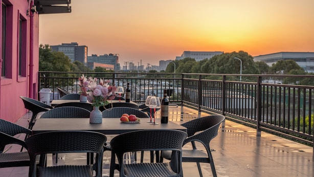 Une terrasse avec une table dressée pour le dîner, agrémentée d’un vase de fleurs et de bouteilles de vin.