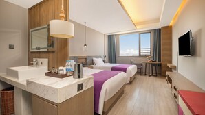 Une chambre d’hôtel avec une salle de bain en marbre, deux lits avec une literie violette, une petite table, un téléviseur et une grande fenêtre avec des rideaux.