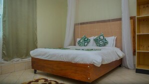 A bedroom with a wooden bed, white bedding, and green patterned pillows. - Ekhaya crescent hotel mbarara (Mbarara)