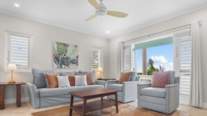 A living room with a sofa, armchair, coffee table, and a ceiling fan. - Greens 2BR (Montego Bay)