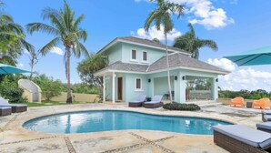 A light blue house with a swimming pool, surrounded by palm trees and outdoor furniture. - Greens 2BR (Montego Bay)