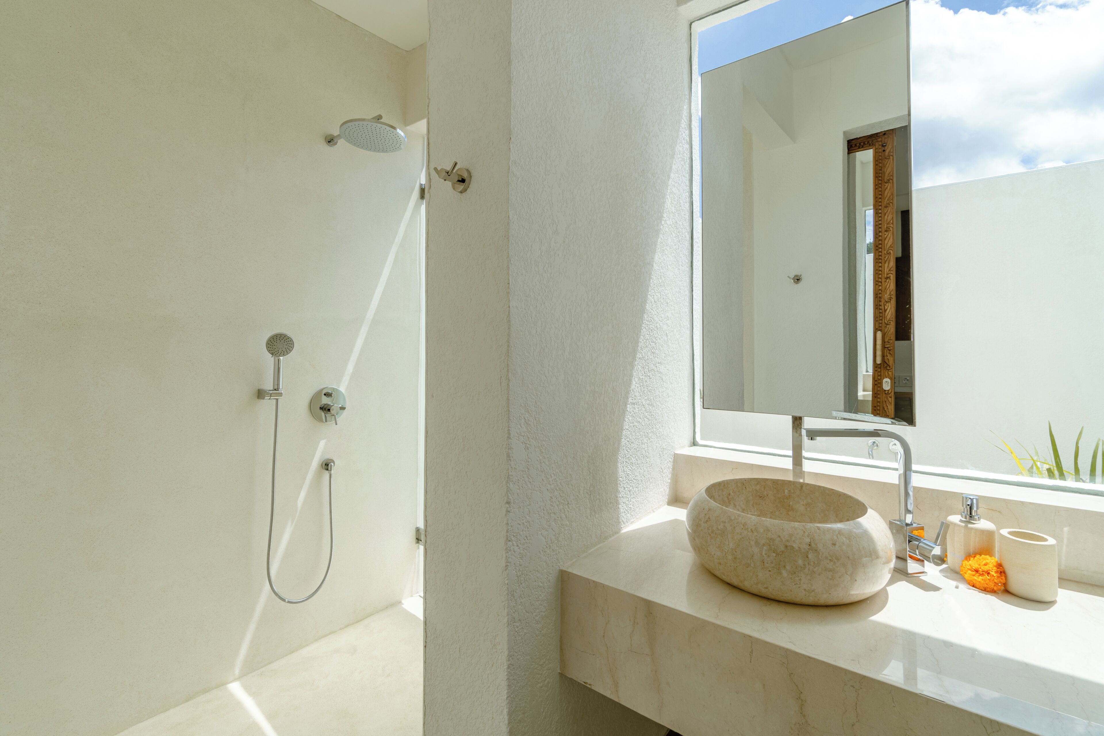 A modern bathroom with a stone sink, a handheld showerhead, and a large mirror.
