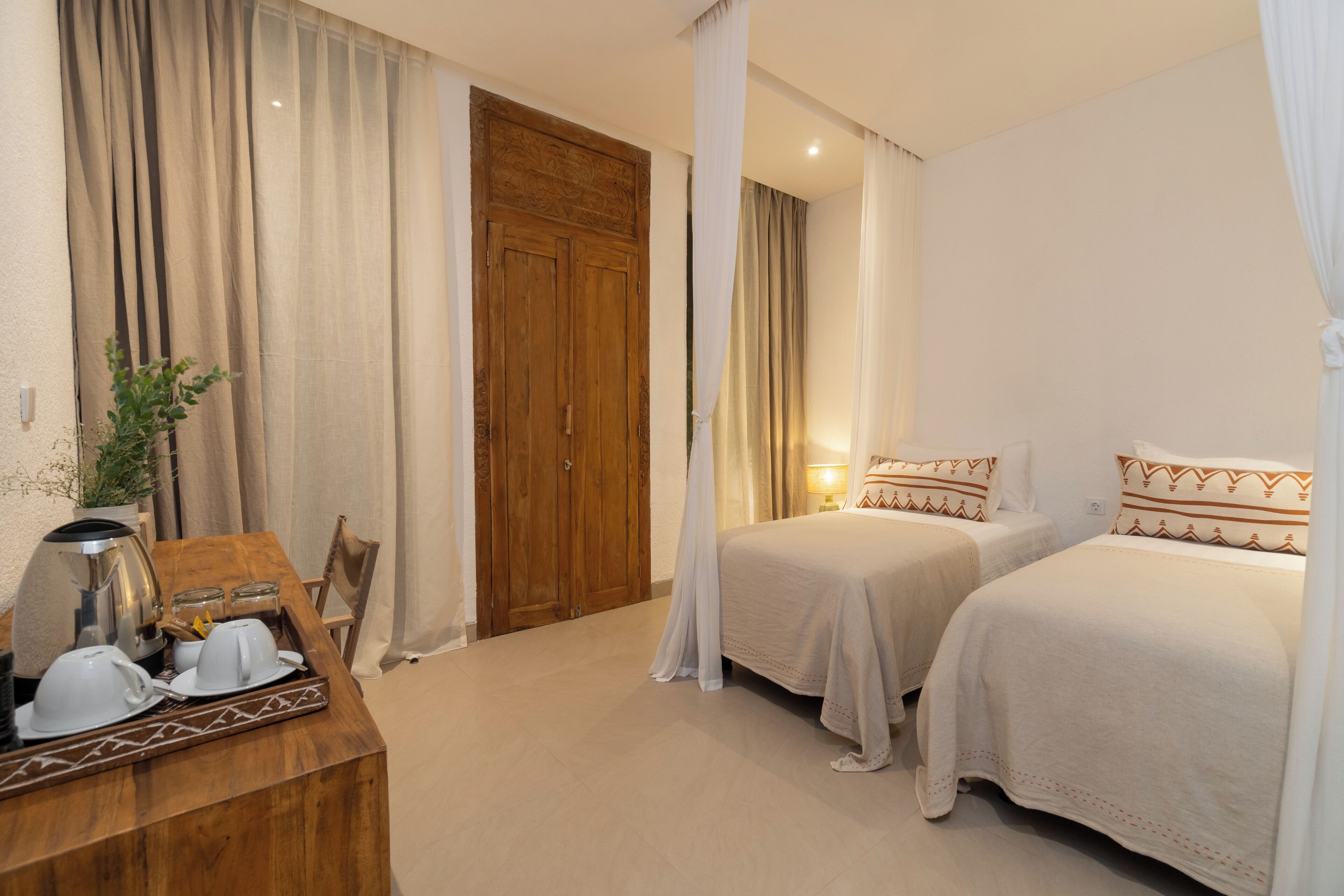 Une chambre d’hôtel avec deux lits, un bureau en bois avec une machine à café et une grande porte en bois.