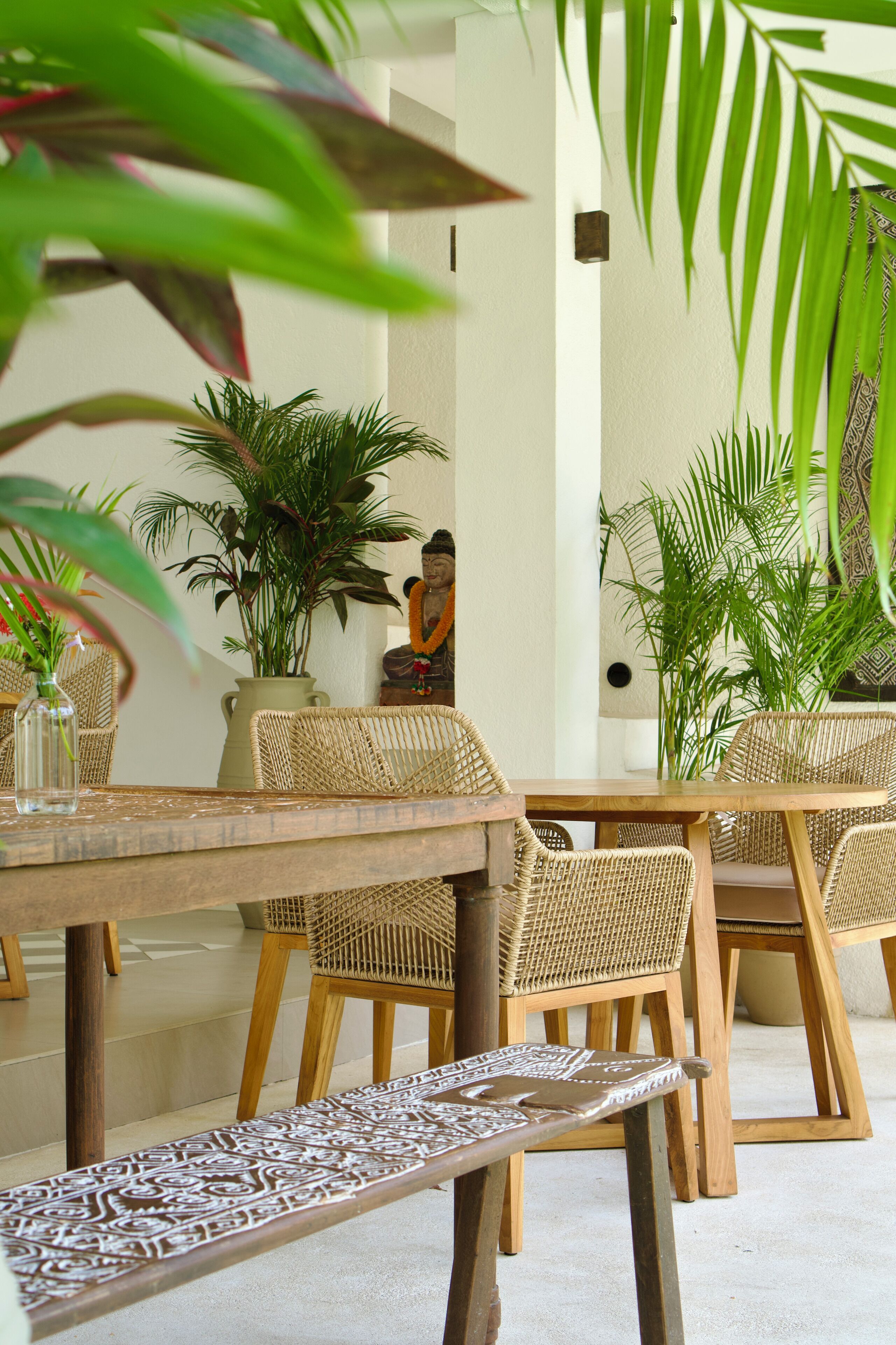Un coin repas avec des meubles en osier, un banc à motifs et des plantes en pot.