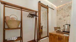 Een houten plank met een rieten mand en paar slippers, een houten tafel met een waterkoker, en een stenen muur.