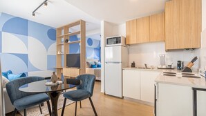 A modern kitchen with white cabinets, a microwave, and a refrigerator. There is a dining area with a round table and two chairs.
