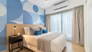 A modern bedroom with a large bed, a nightstand, a wall-mounted air conditioner, and a window with curtains.