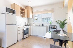 Una cocina moderna con armarios blancos, horno empotrado, microondas y comedor con mesa y sillas de vidrio.