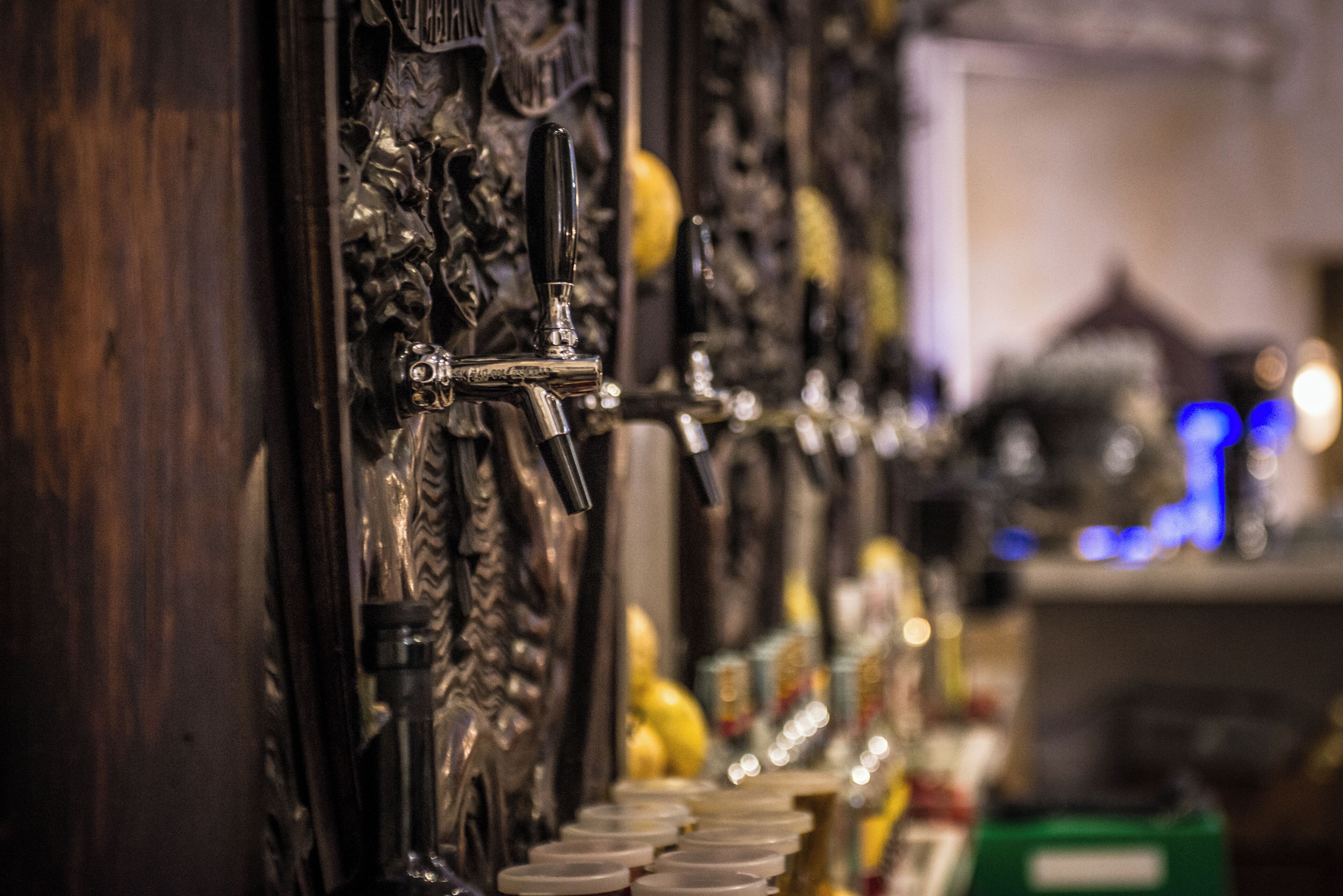 A row of beer taps with ornate carvings on the wall.