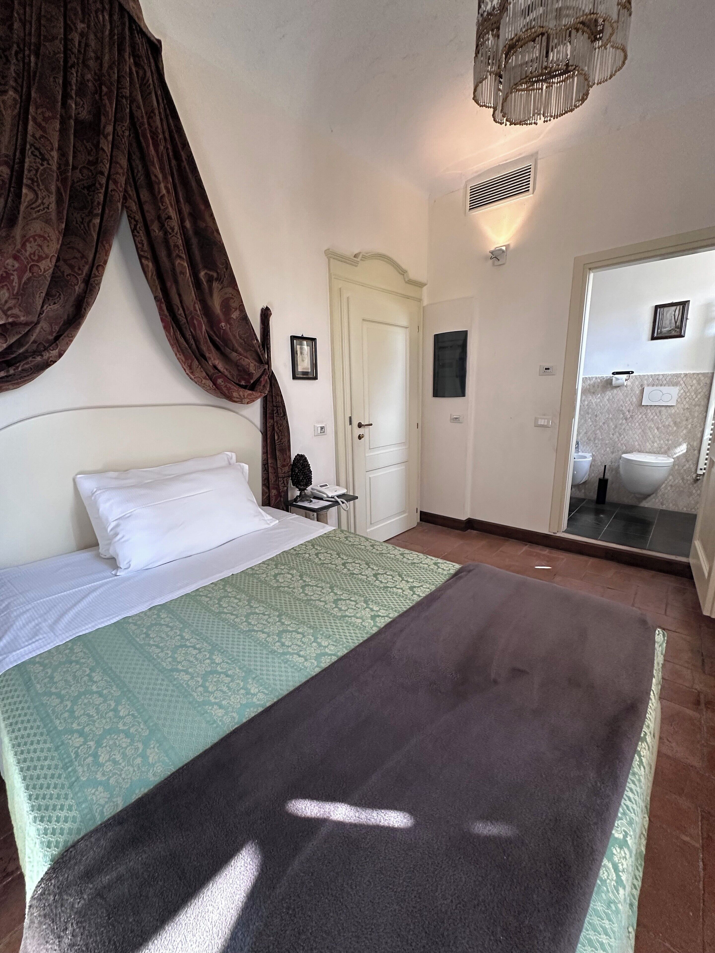 A bedroom with a bed, a nightstand, a door, and a bathroom visible through an open door.