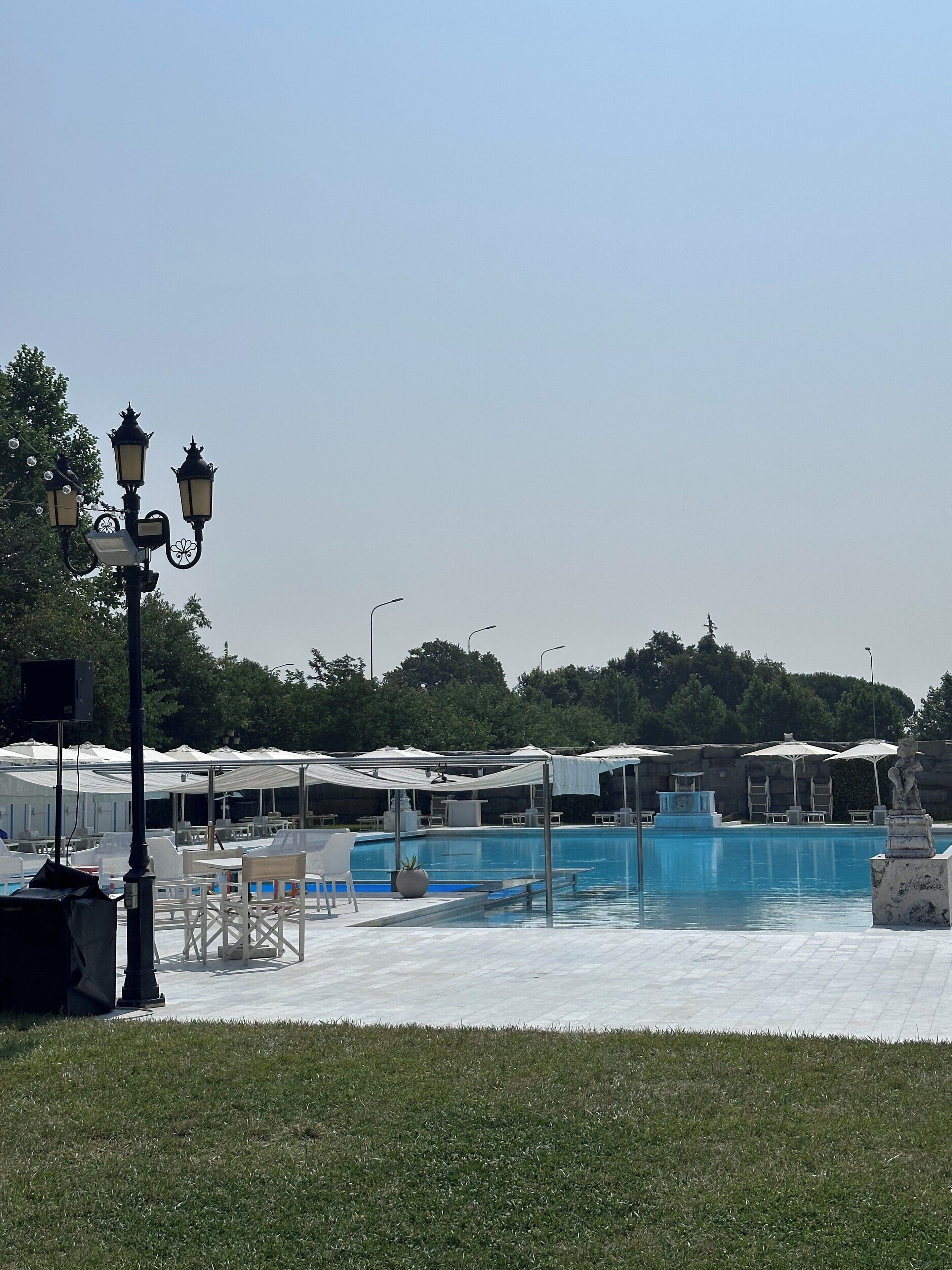A swimming pool area with lounge chairs and umbrellas, surrounded by trees.